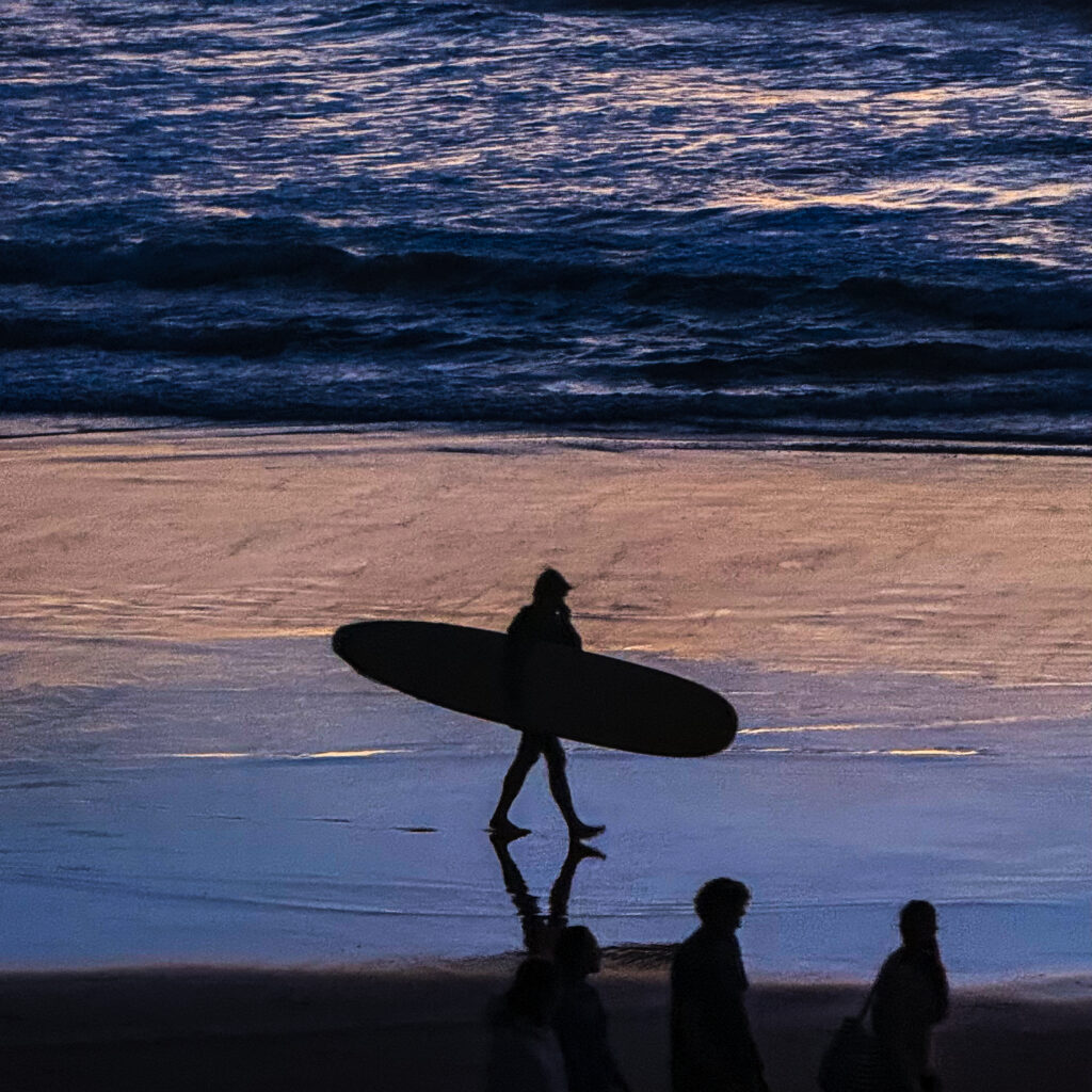 Surfeur marchant sur la plage au coucher du soleil